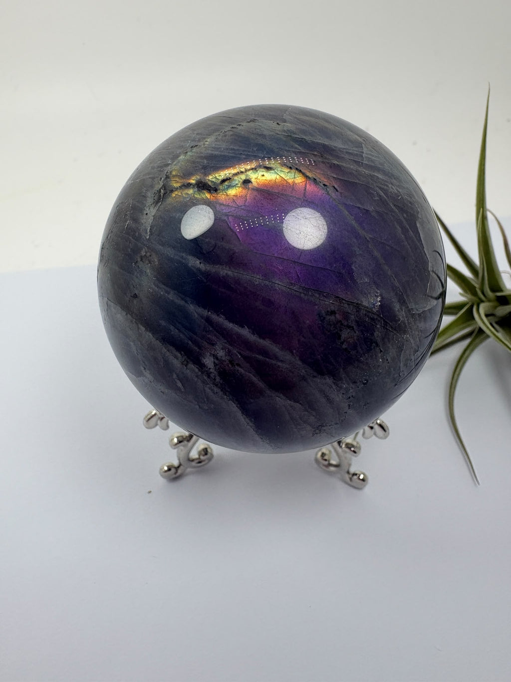 Descubre esta esfera de labradorita pulida con reflejos lilas, violetas y dorados. Recibe la pieza fotografiada. Base no incluida.
