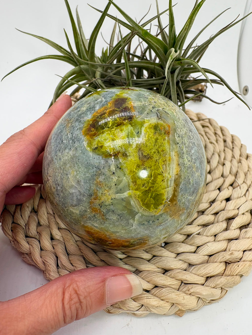 Preciosa esfera de ópalo verde procedente de Madagascar, caracterizada por sus tonalidades verdes, amarillentas y blancas, que forman dibujos naturales únicos en toda la superficie. Su pulido realza el color, el brillo y la riqueza de sus matices.