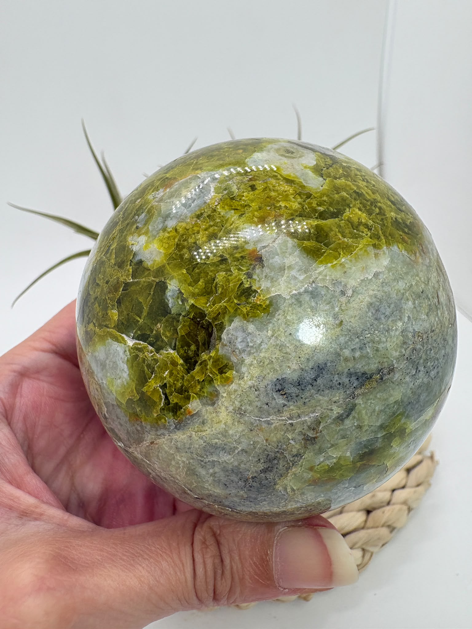 Preciosa esfera de ópalo verde procedente de Madagascar, caracterizada por sus tonalidades verdes, amarillentas y blancas, que forman dibujos naturales únicos en toda la superficie. Su pulido realza el color, el brillo y la riqueza de sus matices.