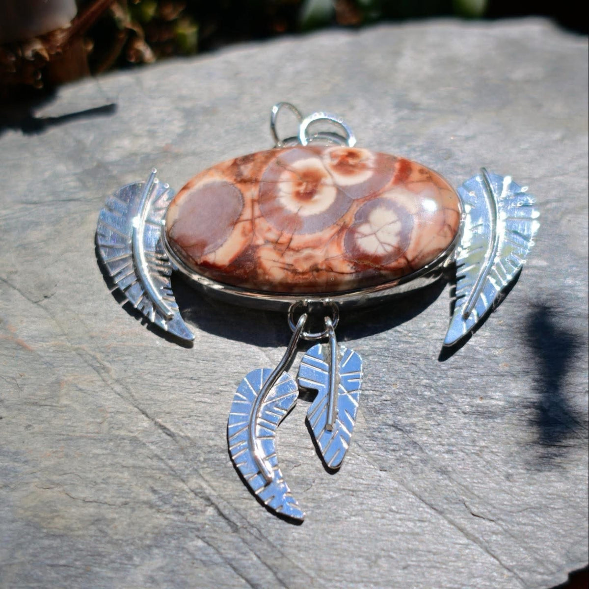 Colgante de plumas con jaspe ojo de pájaro sobre piedra al sol