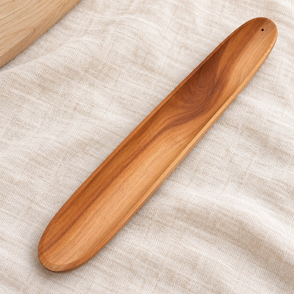 Portaincienso de madera en forma de barca, con vetas naturales y diseño alargado para recoger las cenizas. Medidas: 28,3 × 4 × 1,5 cm.