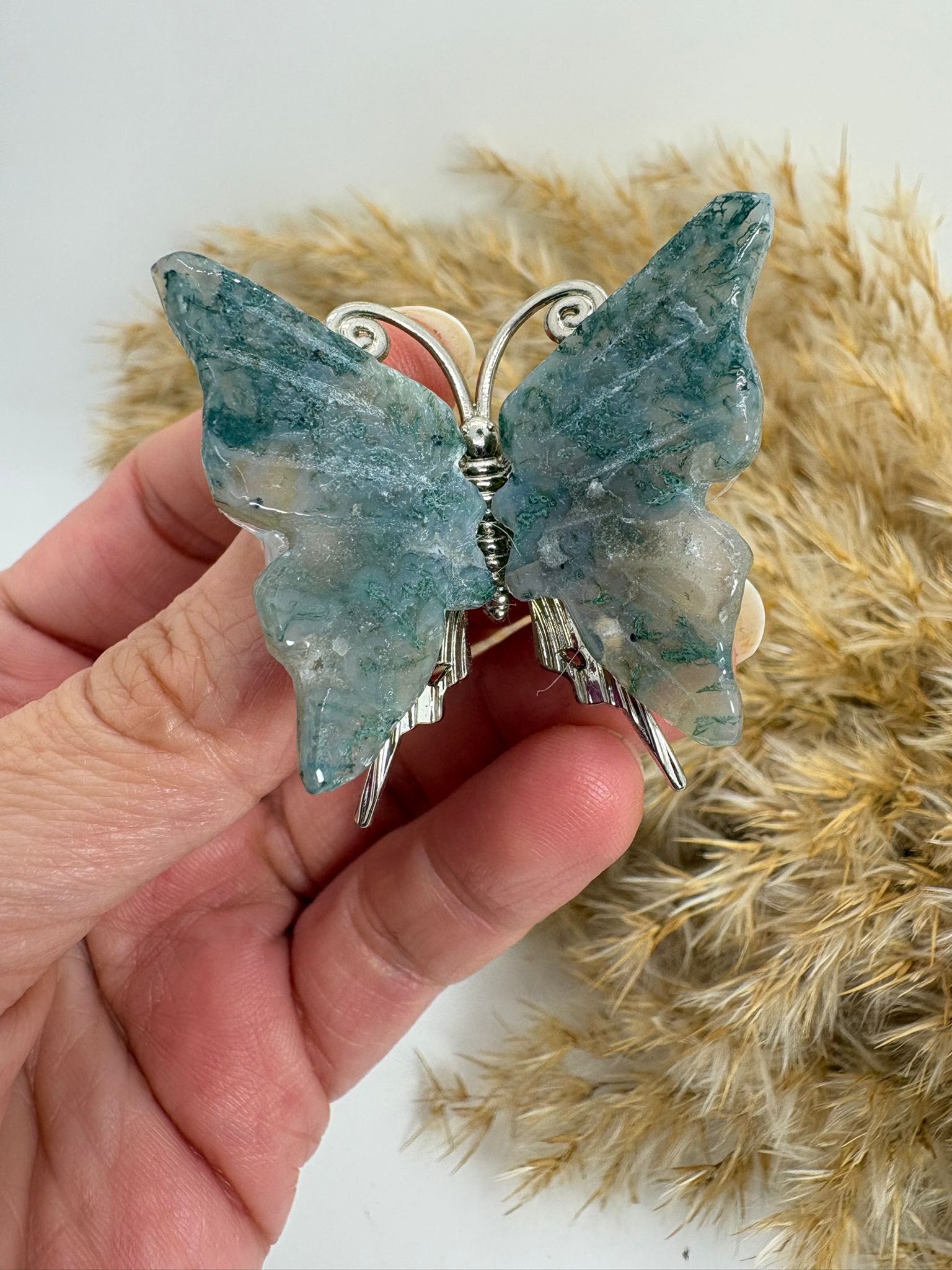 Mariposa de ágata musgo natural tallada, con tonos verdes y dibujos únicos. Pieza decorativa ideal para colección o regalo.