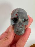Calavera de jaspe heliotropo natural pulida. Mineral con tonos verdes e inclusiones rojizas. Ideal para colección, decoración o regalo especial.