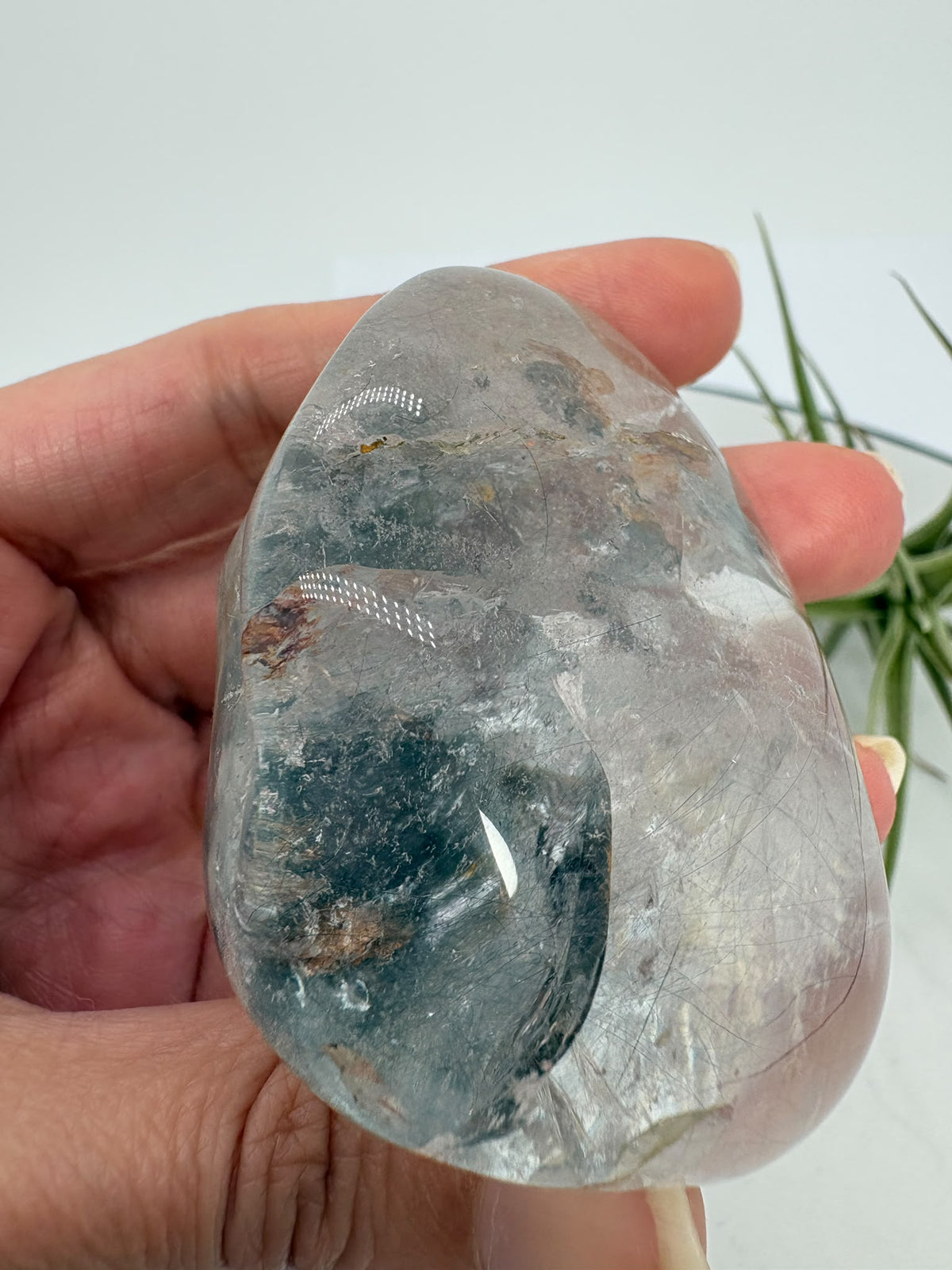 Un pequeño universo natural en el interior del cuarzo. Este palmstone contiene finas agujas de rutilo e inclusiones de aspecto plateado, que crean un paisaje lleno de detalles entre transparencias y delicados matices cálidos.