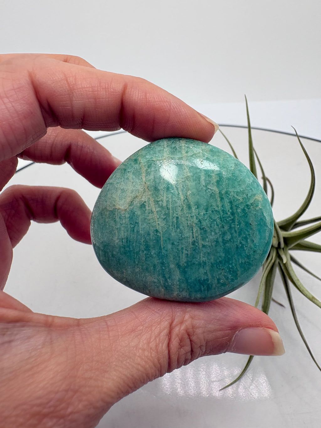 palmstone de amazonita natural pulida con inclusiones de cuarzo ahumado y mica biotita, de Madagascar.

&nbsp;Una piedra perfecta para llevar en la mano, meditar o utilizar como apoyo energético diario. La amazonita destaca por sus tonos verde azulados con vetas naturales más oscuras, que le aportan profundidad y un aspecto único.