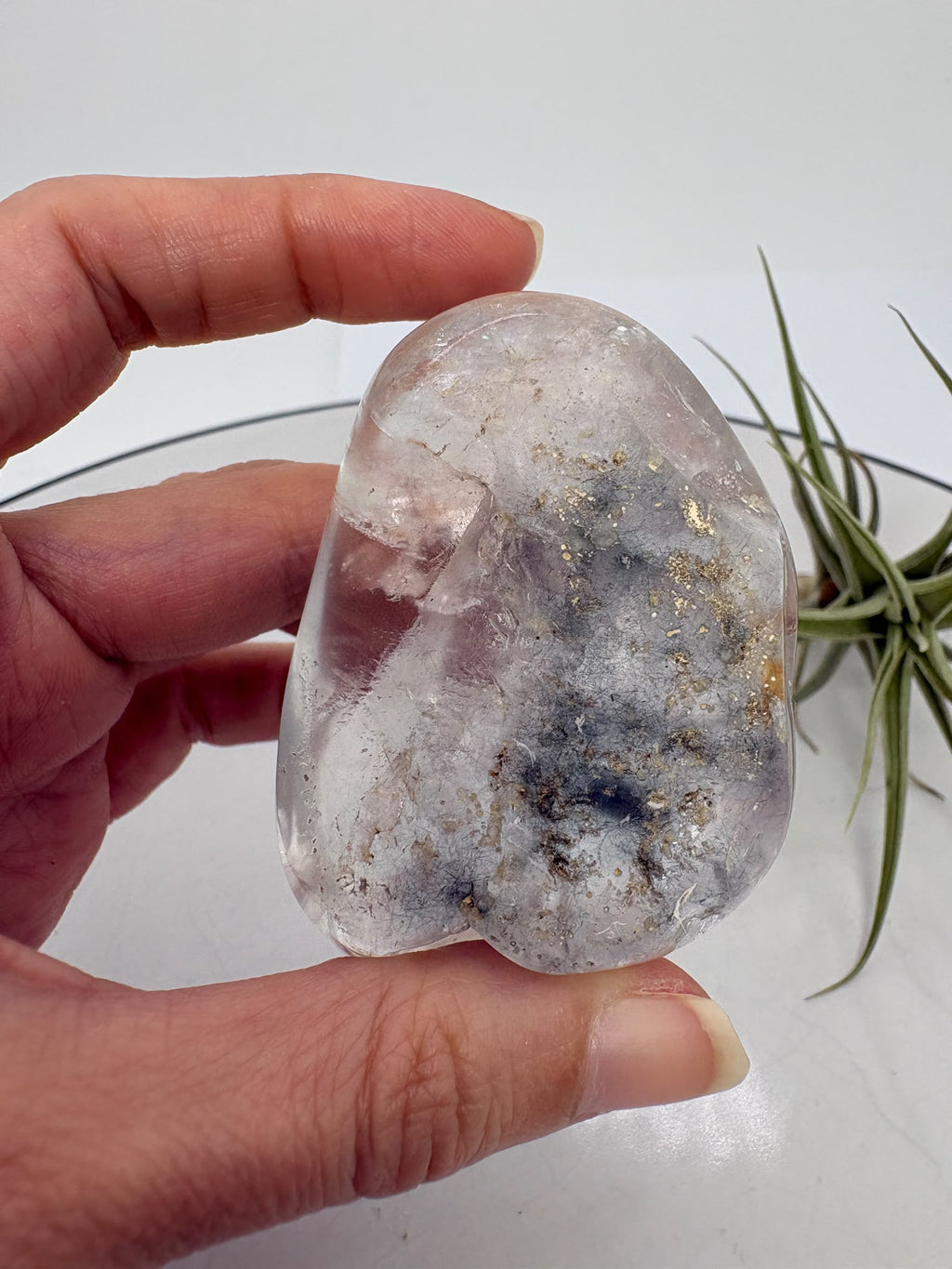 Un pequeño universo natural en el interior del cuarzo. Este palmstone contiene finas agujas de rutilo e inclusiones de aspecto plateado, que crean un paisaje lleno de detalles entre transparencias y delicados matices cálidos.