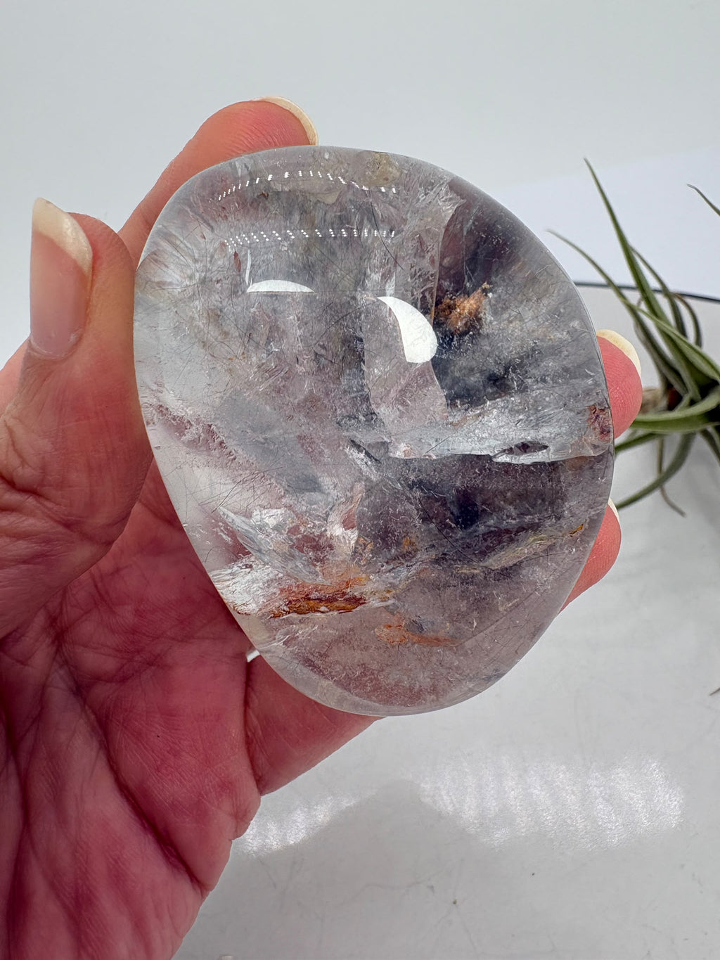 Un pequeño universo natural en el interior del cuarzo. Este palmstone contiene finas agujas de rutilo e inclusiones de aspecto plateado, que crean un paisaje lleno de detalles entre transparencias y delicados matices cálidos.