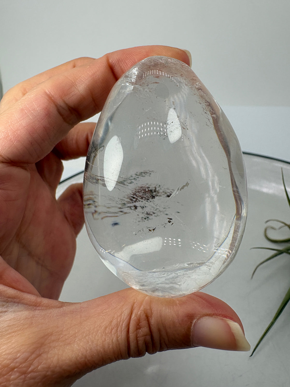 Huevo de cuarzo muy cristalino con inclusiones de lodolita en su interior. Su transparencia permite apreciar pequeños detalles en tonos rojizos y terrosos, como un diminuto paisaje suspendido dentro del cristal. Una pieza para observar de cerca y descubrir desde diferentes ángulos.