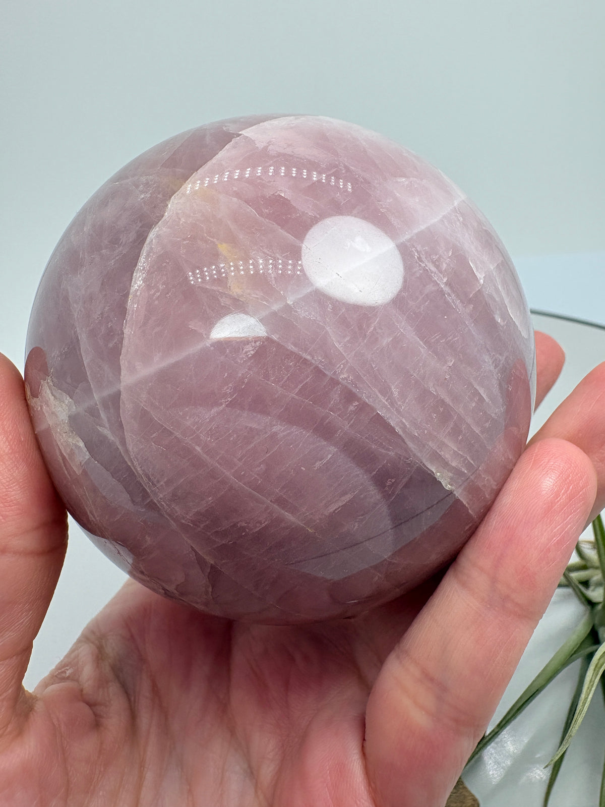 Una preciosa esfera de cuarzo rosa con zonas translúcidas y delicados velos blancos que recorren su interior. Su superficie pulida permite apreciar los distintos matices del mineral, creando una pieza llena de detalles para decorar un rincón especial o regalar con cariño.