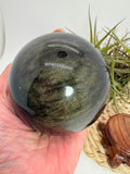 Esfera de obsidiana dorada procedente de México, de gran tamaño y con un intenso acabado pulido. Su superficie oscura revela preciosos reflejos dorados al recibir la luz, creando un efecto brillante y profundo característico de esta variedad de obsidiana.