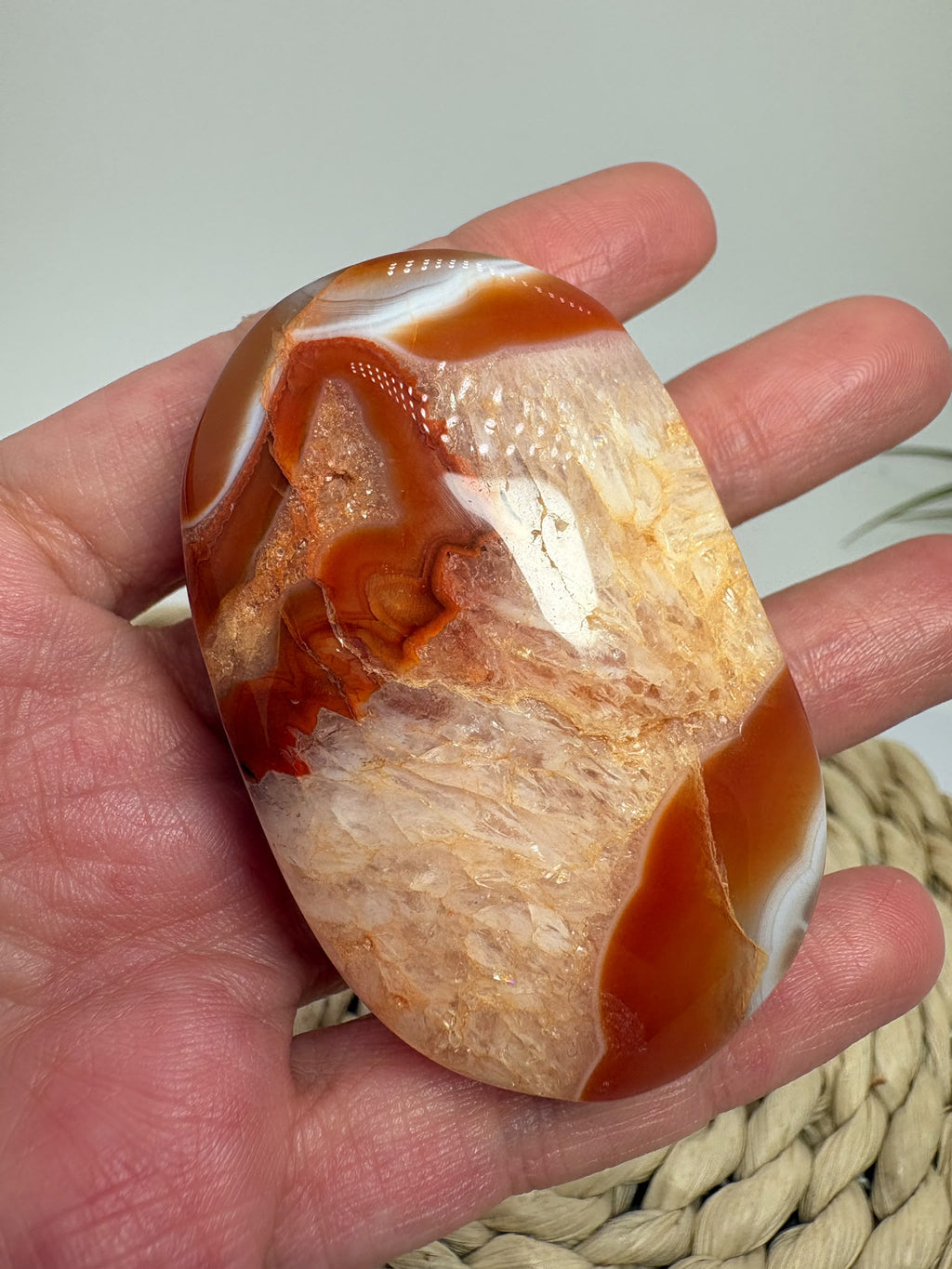 Descubre esta palmstone de ágata cornalina pulida, con bandas rojizas y tonos crema. Recibe la pieza fotografiada de La Hada de las Piedras.