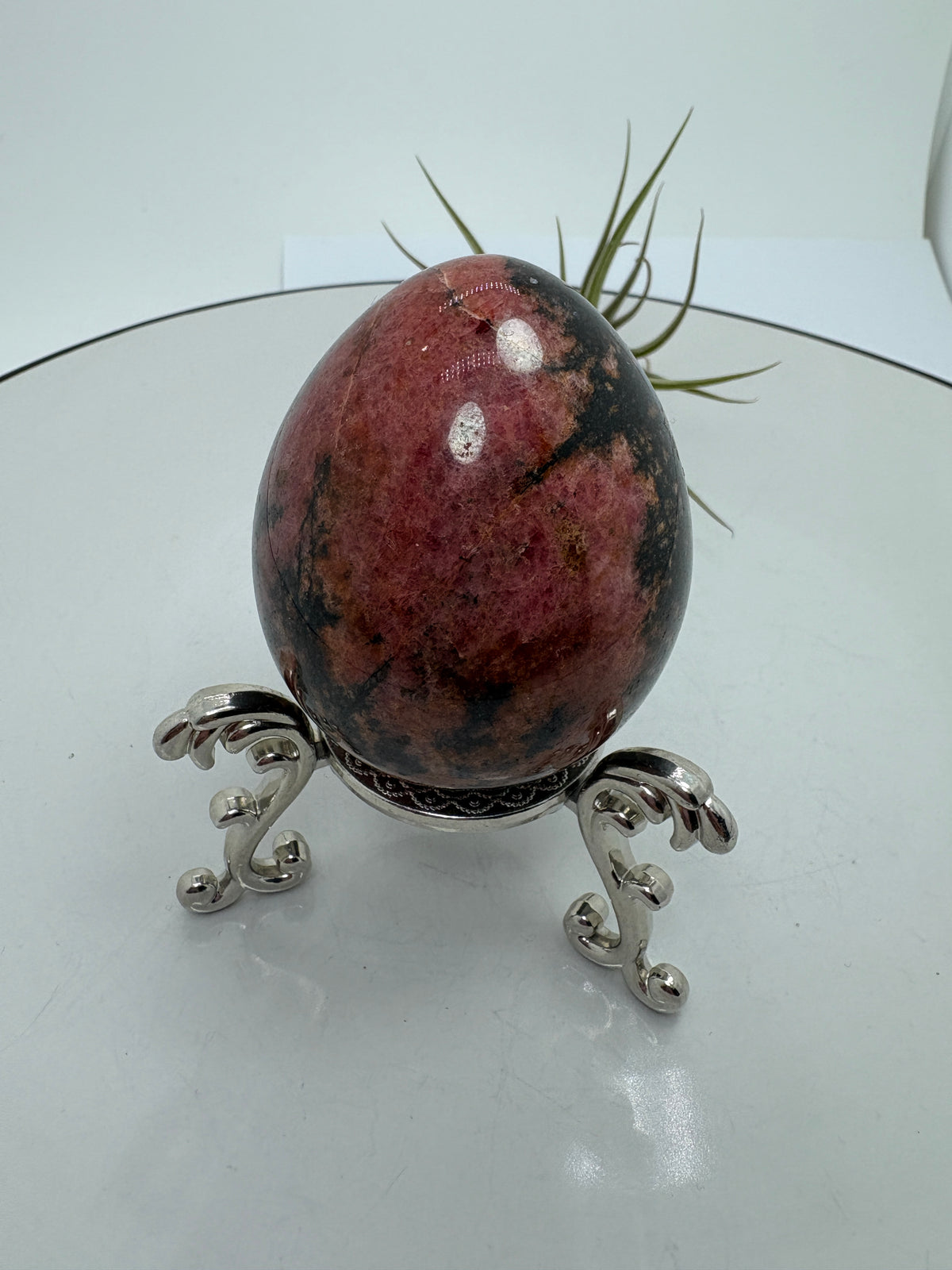 Un precioso huevo de rodonita que combina tonos rosa intenso con zonas negras y matices terrosos. Sus dibujos cambian en cada cara, mostrando una parte más rosada y otra más oscura, con un contraste que le da mucha personalidad. El acabado pulido realza sus colores y su brillo natural.