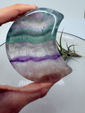 Una pequeña bandeja de fluorita arcoíris tallada en forma de luna, perfecta para colocar tus anillos, pendientes o algún pequeño mineral. Una pieza bonita y especial para tu mesita de noche, tocador o rincón de meditación.