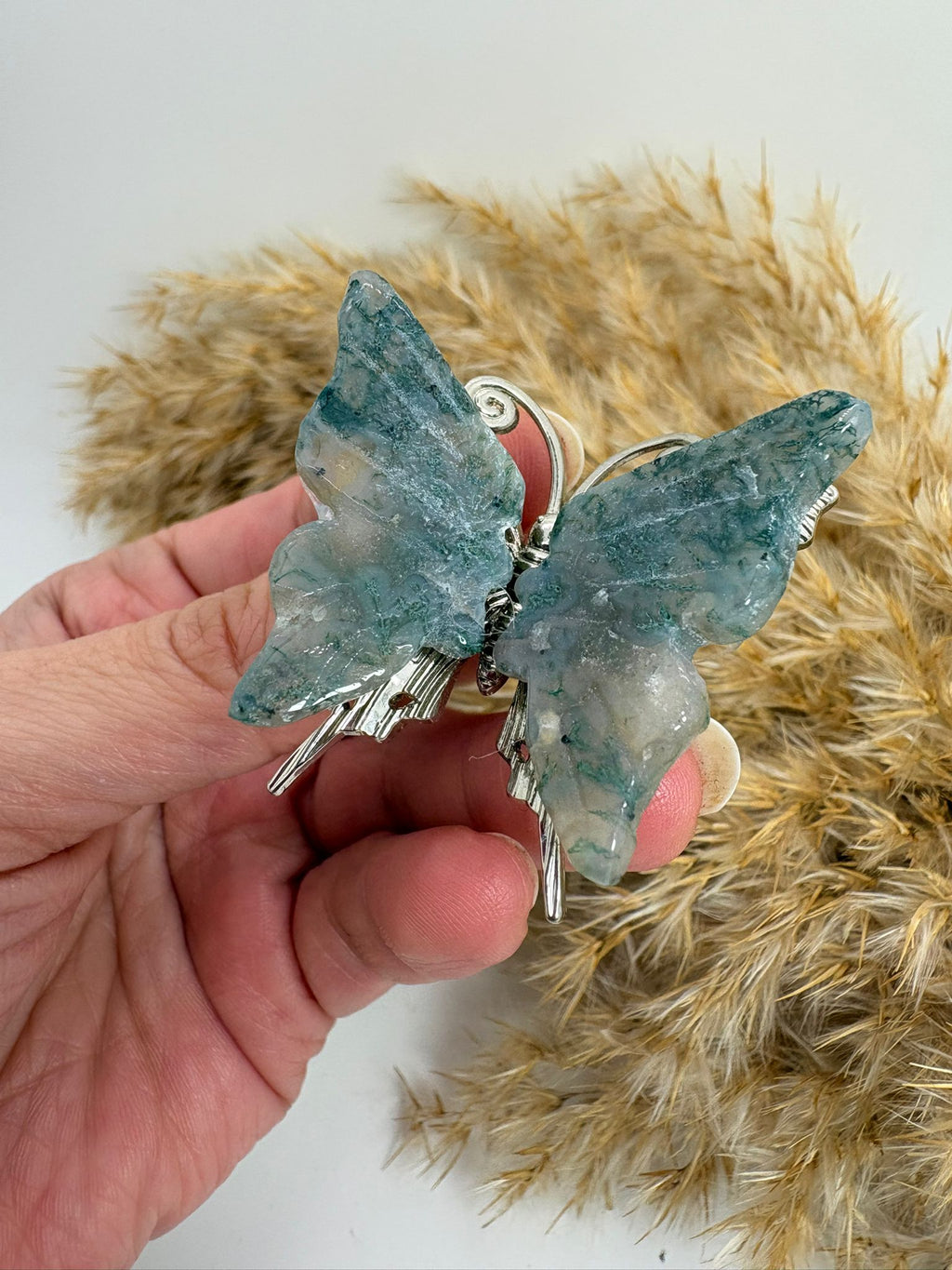 Mariposa de ágata musgo natural tallada, con tonos verdes y dibujos únicos. Pieza decorativa ideal para colección o regalo.