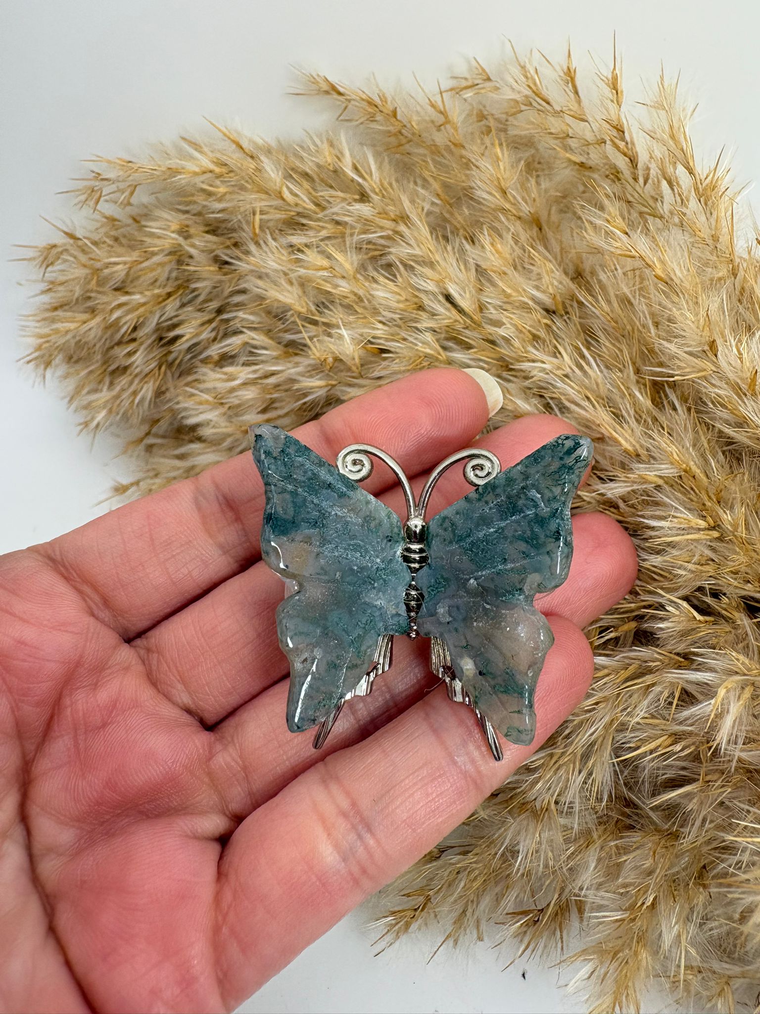 Mariposa de ágata musgo natural tallada, con tonos verdes y dibujos únicos. Pieza decorativa ideal para colección o regalo.