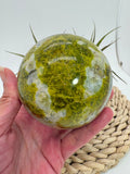 Preciosa esfera de ópalo verde procedente de Madagascar, caracterizada por sus tonalidades verdes, amarillentas y blancas, que forman dibujos naturales únicos en toda la superficie. Su pulido realza el color, el brillo y la riqueza de sus matices.