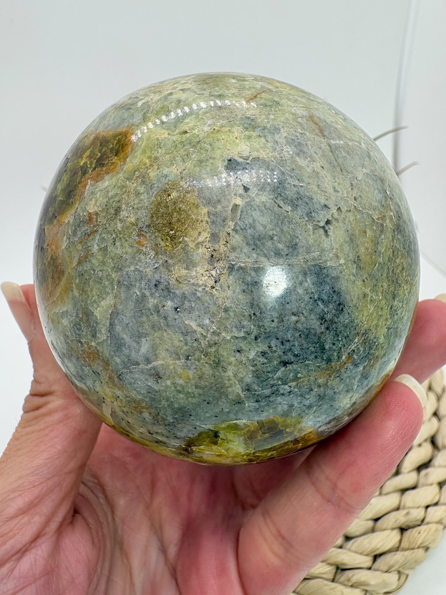 Preciosa esfera de ópalo verde procedente de Madagascar, caracterizada por sus tonalidades verdes, amarillentas y blancas, que forman dibujos naturales únicos en toda la superficie. Su pulido realza el color, el brillo y la riqueza de sus matices.