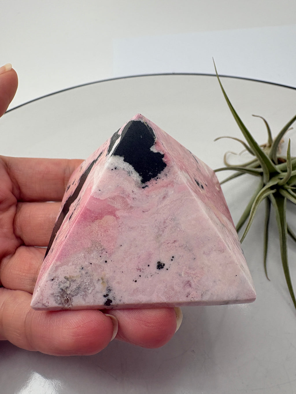 Pirámide de rodonita de Perú con una bonita combinación de tonos rosas, zonas claras y manchas negras que destacan sobre su superficie pulida. Sus dibujos naturales hacen de ella una pieza única, ideal para decorar un rincón especial o ampliar tu colección de minerales.