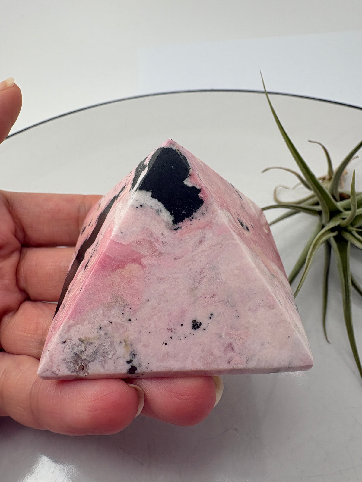 Pirámide de rodonita de Perú con una bonita combinación de tonos rosas, zonas claras y manchas negras que destacan sobre su superficie pulida. Sus dibujos naturales hacen de ella una pieza única, ideal para decorar un rincón especial o ampliar tu colección de minerales.