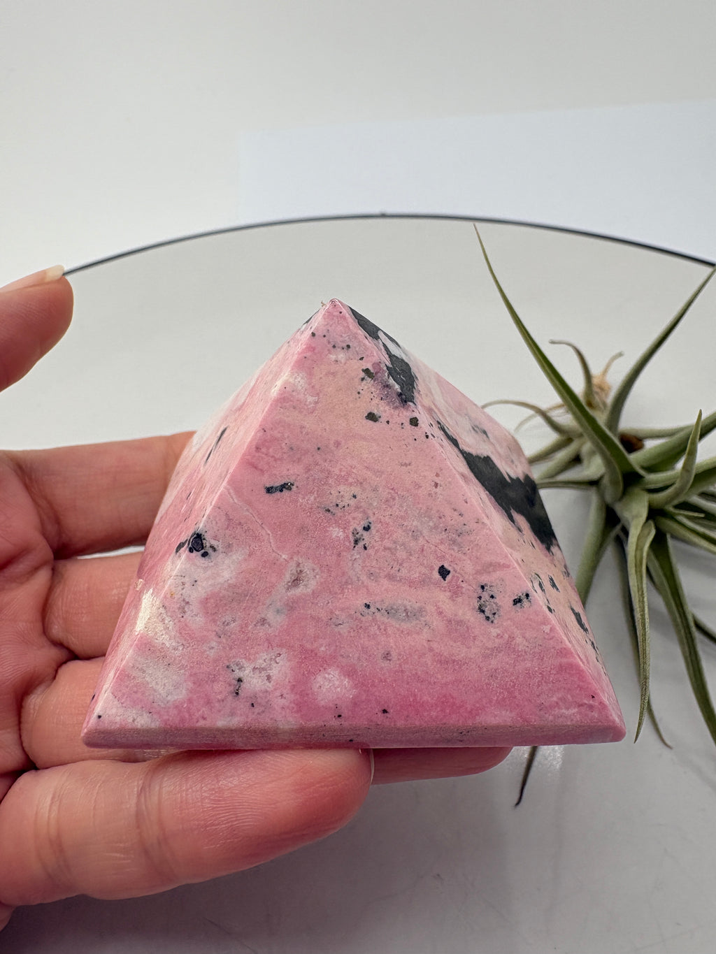 Pirámide de rodonita de Perú con una bonita combinación de tonos rosas, zonas claras y manchas negras que destacan sobre su superficie pulida. Sus dibujos naturales hacen de ella una pieza única, ideal para decorar un rincón especial o ampliar tu colección de minerales.