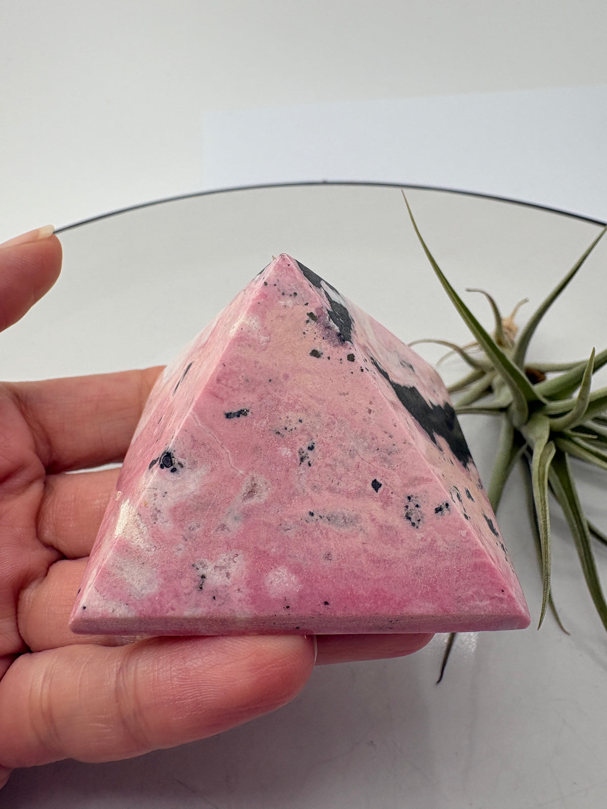 Pirámide de rodonita de Perú con una bonita combinación de tonos rosas, zonas claras y manchas negras que destacan sobre su superficie pulida. Sus dibujos naturales hacen de ella una pieza única, ideal para decorar un rincón especial o ampliar tu colección de minerales.