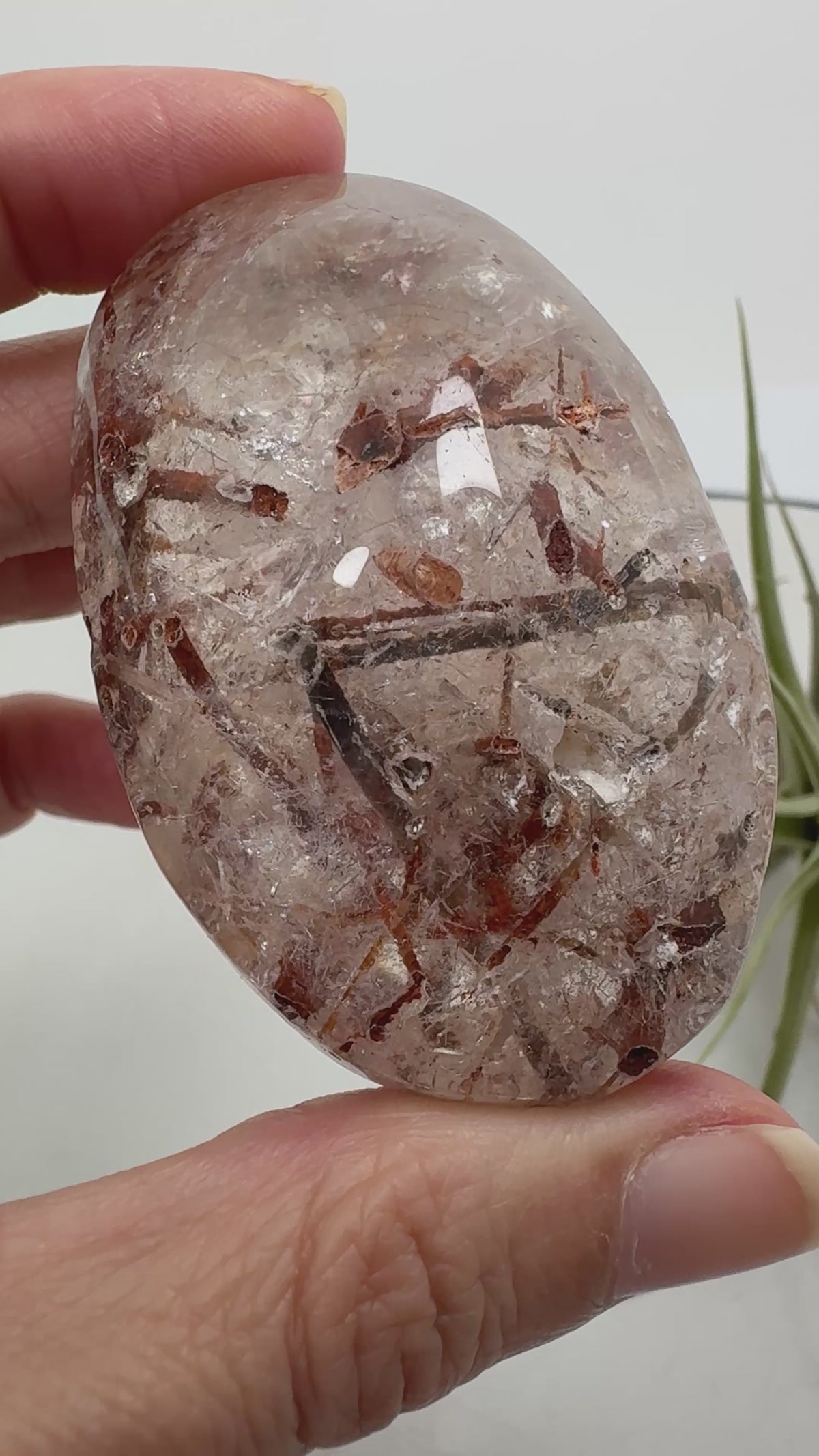 Un pequeño paisaje mineral en la palma de tu mano. Este palmstone de cuarzo con anfíbol destaca por sus inclusiones en tonos verdes oscuros, marrones y rojizos, que crean formas y contrastes únicos en su interior.

La transparencia del cuarzo permite descubrir distintos detalles al observarlo desde diferentes ángulos. Su acabado semipulido combina zonas suaves y brillantes con una textura más natural.