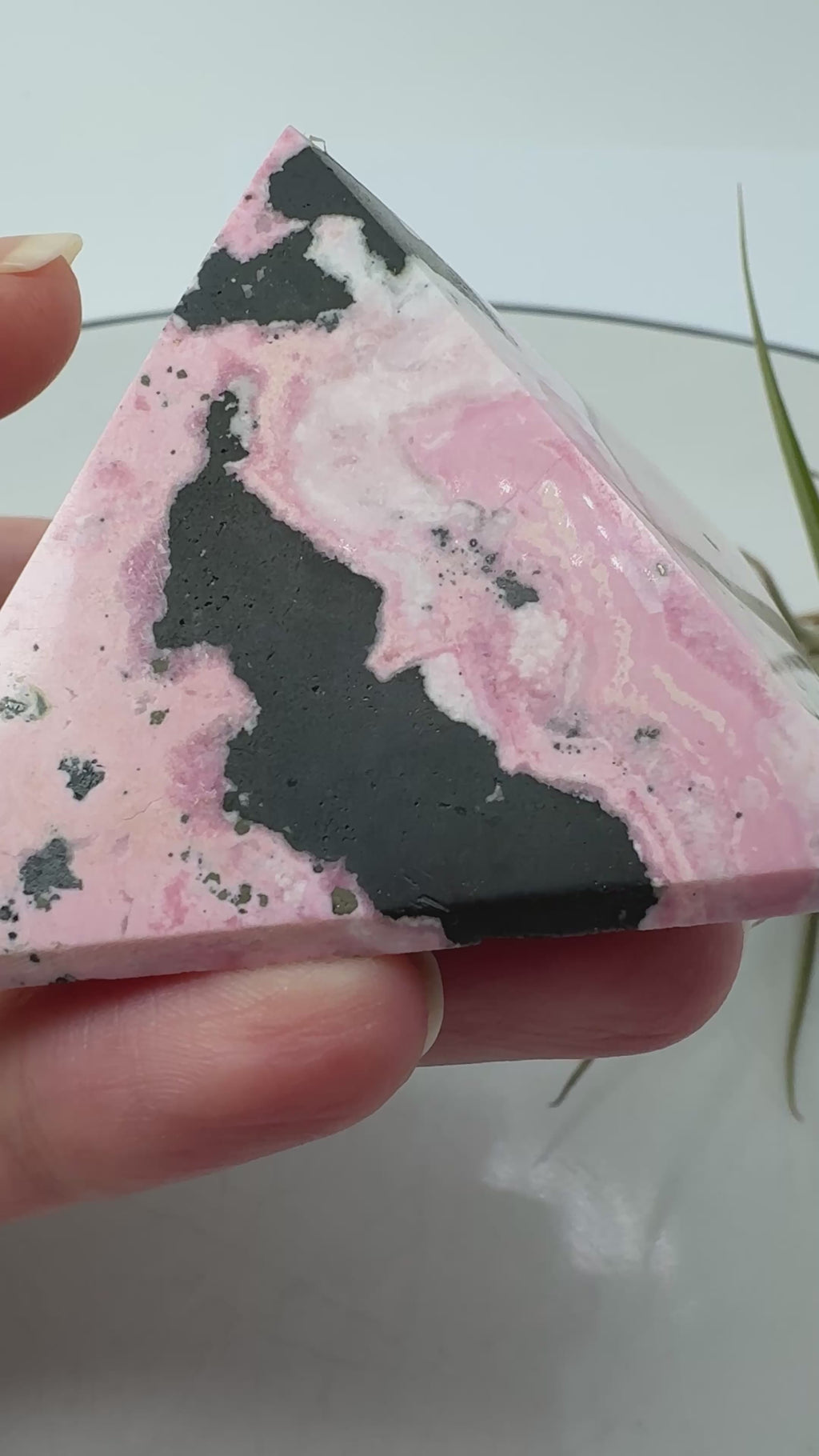 Pirámide de rodonita de Perú con una bonita combinación de tonos rosas, zonas claras y manchas negras que destacan sobre su superficie pulida. Sus dibujos naturales hacen de ella una pieza única, ideal para decorar un rincón especial o ampliar tu colección de minerales.