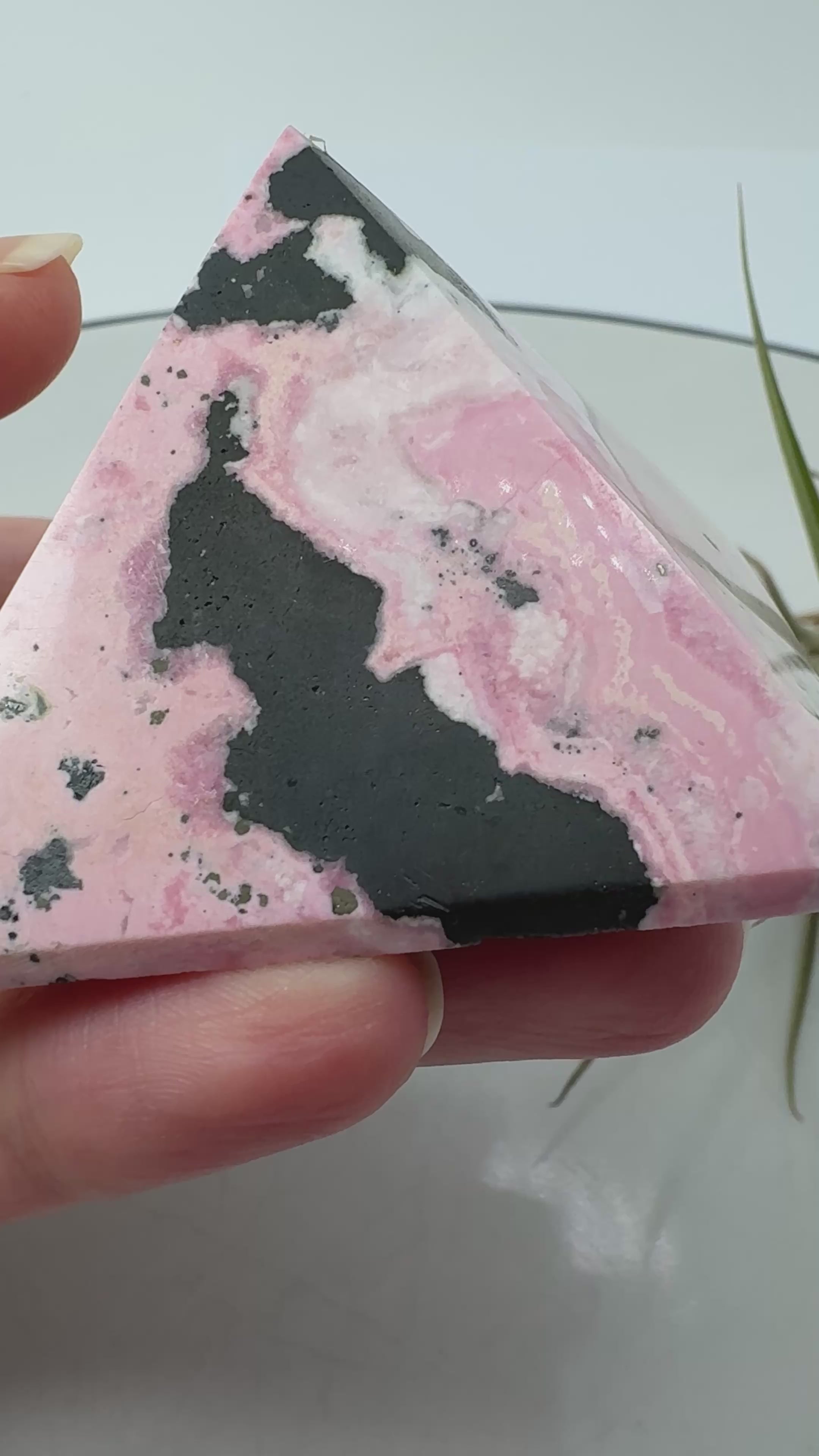Pirámide de rodonita de Perú con una bonita combinación de tonos rosas, zonas claras y manchas negras que destacan sobre su superficie pulida. Sus dibujos naturales hacen de ella una pieza única, ideal para decorar un rincón especial o ampliar tu colección de minerales.